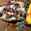 A pizza made with Conservation Grains' MT Neo Pizza flour next to a slice of canteloupe. A sprig of purple flours in the foreground